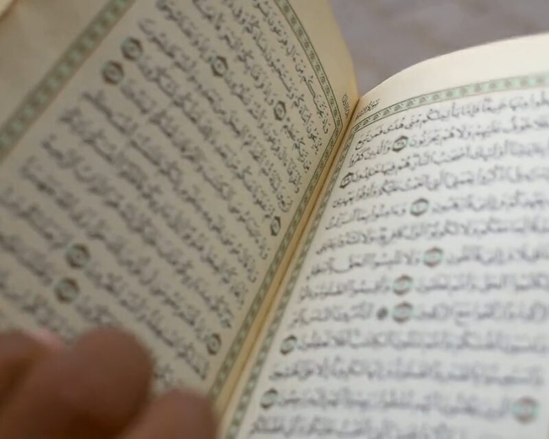 Een opengeslagen mushaf, een hand rust naast de tekst