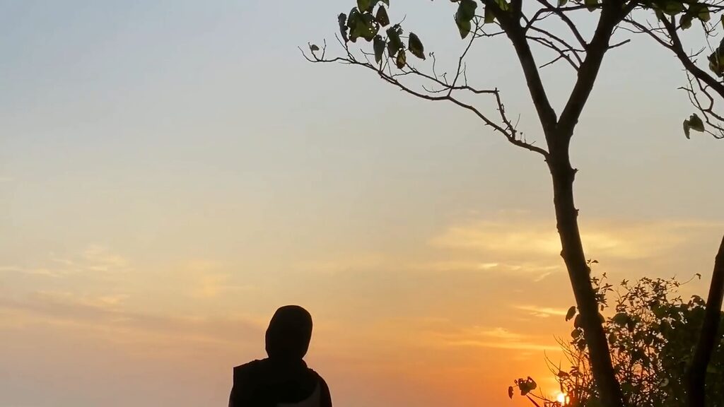 Een silhouet zit onder een boom terwijl de zon laag staat, het gouden uur